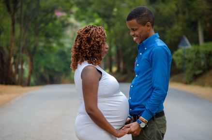 smiling man facing and holding hands of pregnant woman